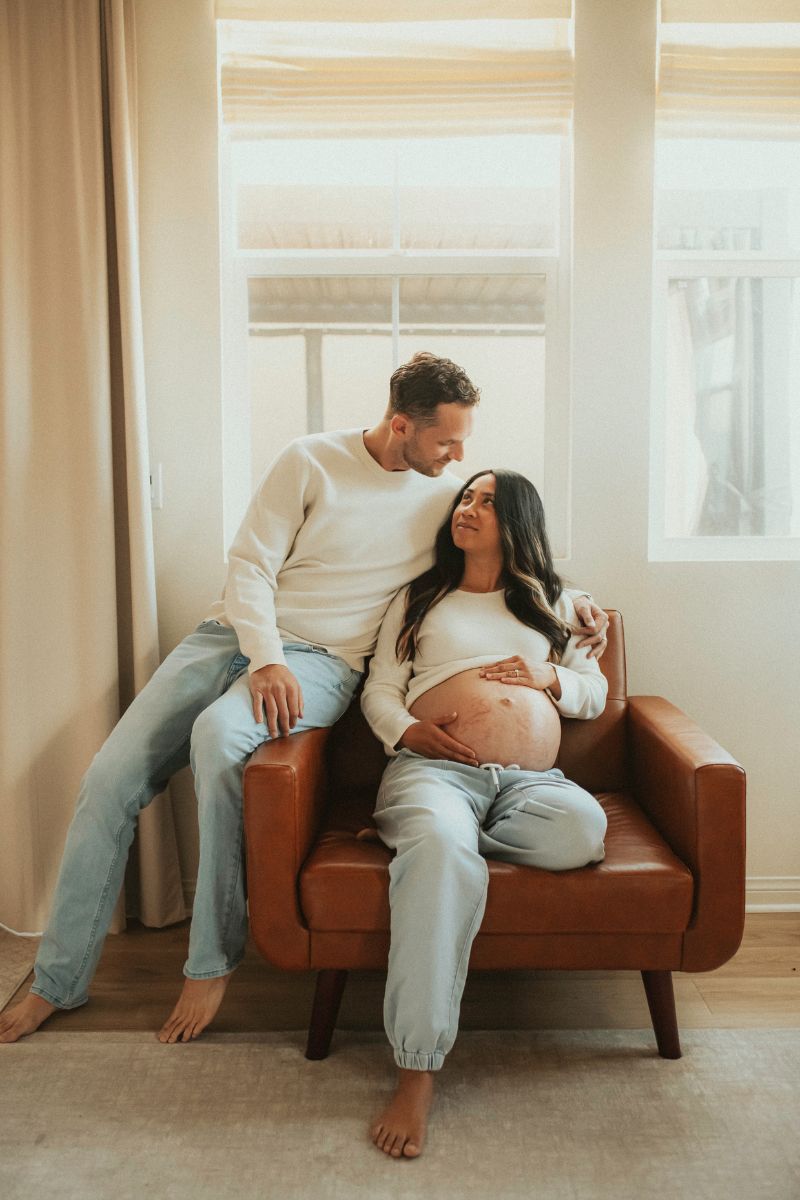 Couple that is expecting a new baby posing for a picture on the couch