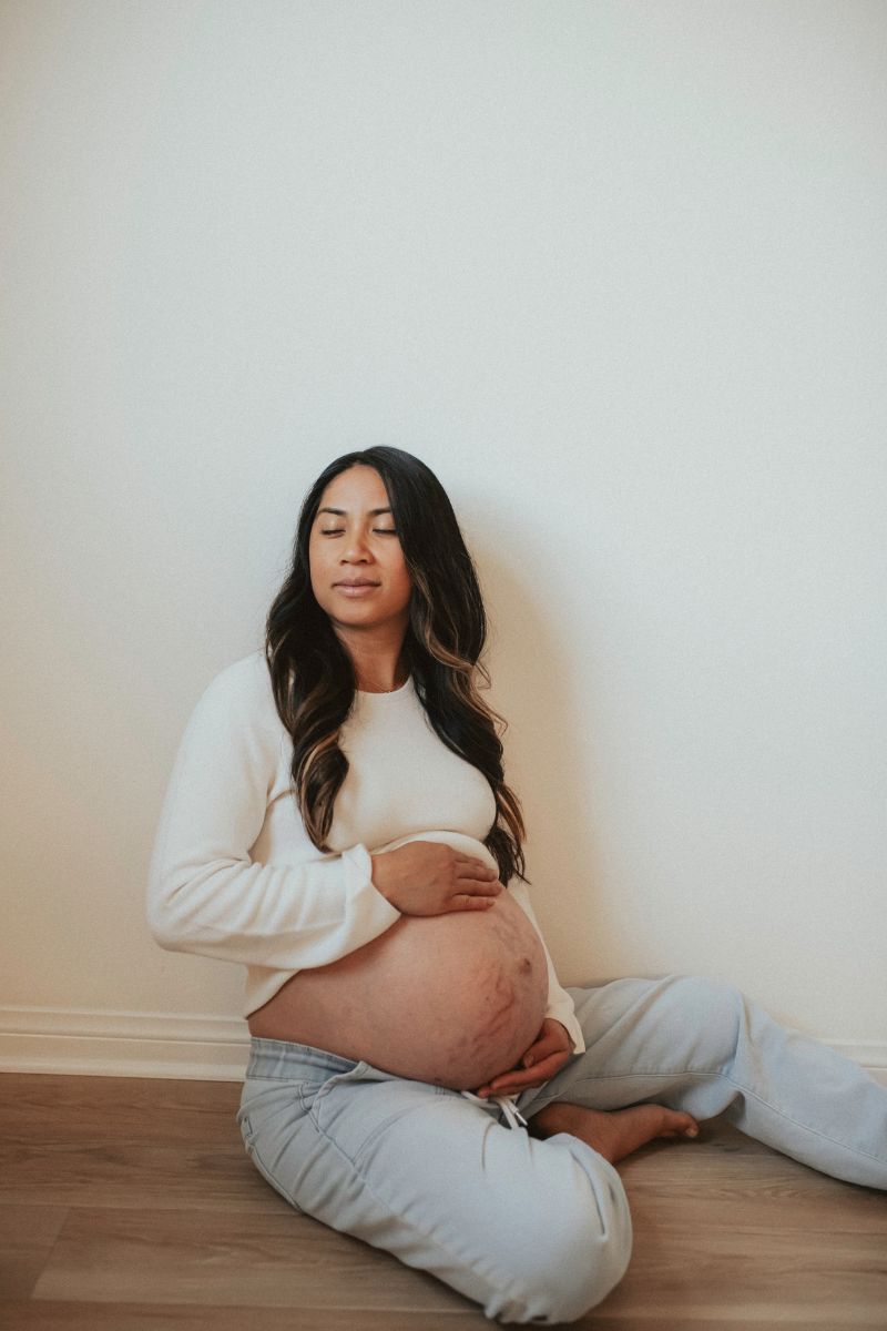 Expecting mom in jeans and a white top sitting on the floor cross legged