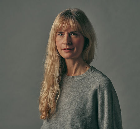 "Sara Skoglund står upp mot en grå bakgrund och tittar in i kameran med ett vänligt leende.