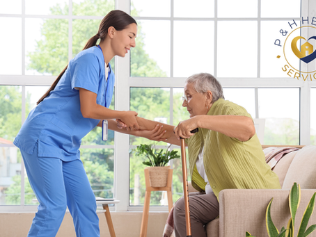 A professional caregiver in blue scrubs gently assists an older woman using a cane as she stands from a chair at home, representing compassionate senior home care and daily living support from P&H Health Services.
