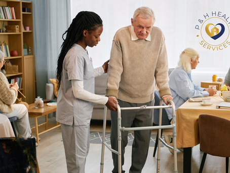 A professional caregiver assists an elderly man using a walker in a bright, welcoming senior living environment while other older adults socialize and enjoy activities in the background. The image highlights compassionate, personalized mobility support and companionship, with the P&H Health Services logo displayed in the upper-right corner.