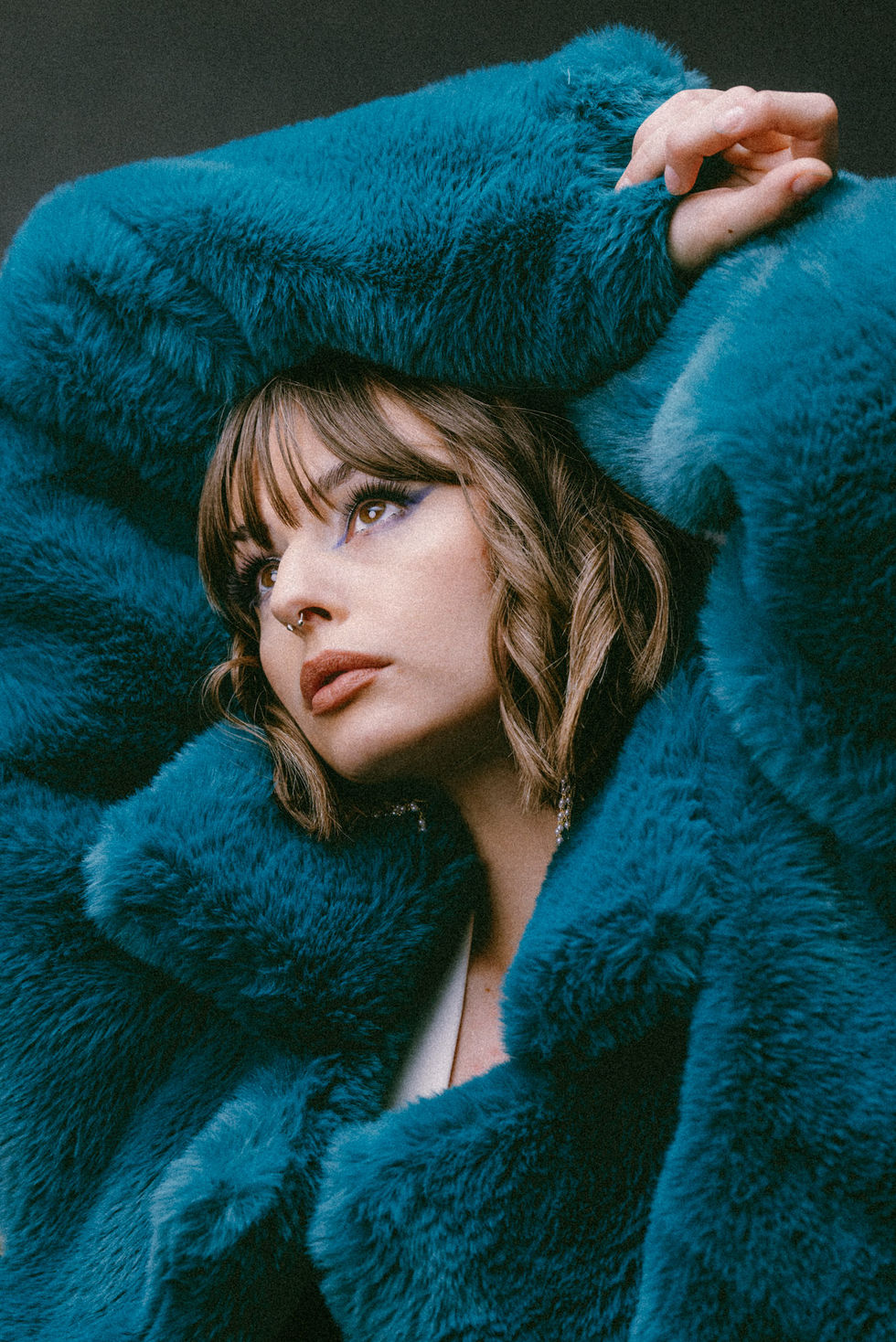 Color portrait of a woman looking upward, a teal fur coat draped over her head and shoulder.