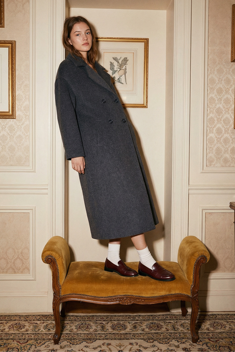 Image générée par IA : mannequin en manteau vert foncé debout sur un banc, intérieur chic.