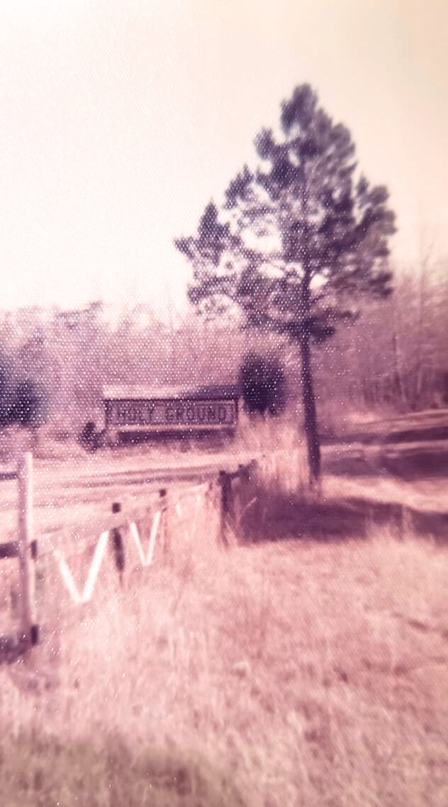 field with a sign in the distance with a tree and small fence.