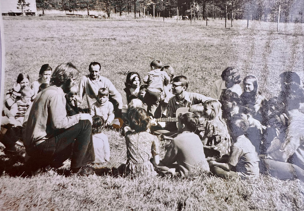 A large group of people sitting in a circle on the ground. A man in the middle of the group is playing the guitar.