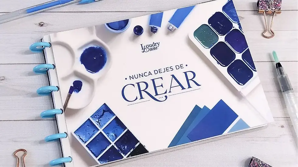 Cuaderno de lettering con la frase “Nunca dejes de crear” en la portada, rodeado de acuarelas, pinceles y materiales de arte en tonos azules.