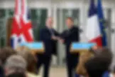 Keir Starmer y Emmanuel Macron se estrechan la mano sonrientes frente a atriles y banderas de Reino Unido y Francia.