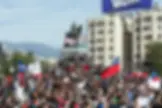 Varias personas marchan al atardecer portando banderas coloridas y rodeadas de humo durante una manifestación.