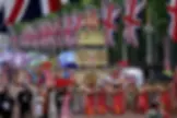 Personas bailan con trajes coloridos junto a una carroza decorada, ondean banderas del Reino Unido en un desfile festivo.