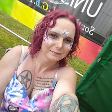 A picture of Skye, a director of CrawleyLGBT. She is taking a selfie in front of a rainbow banner with Unison written on it. Skye has flowers painted on her face.