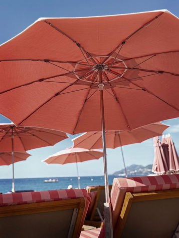 Photograph of orange parasols and beach chairs facing the blue Mediterranean sea on the Côte d’Azur.