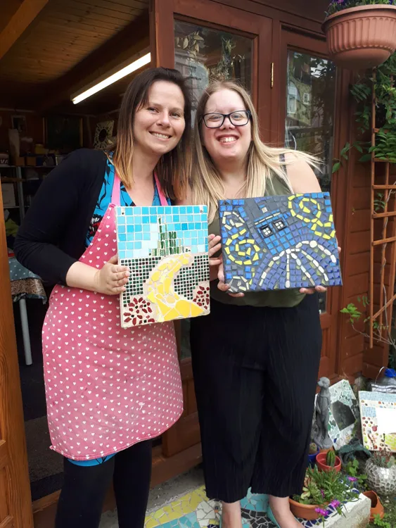 two women proudly holding their completed mosaics
