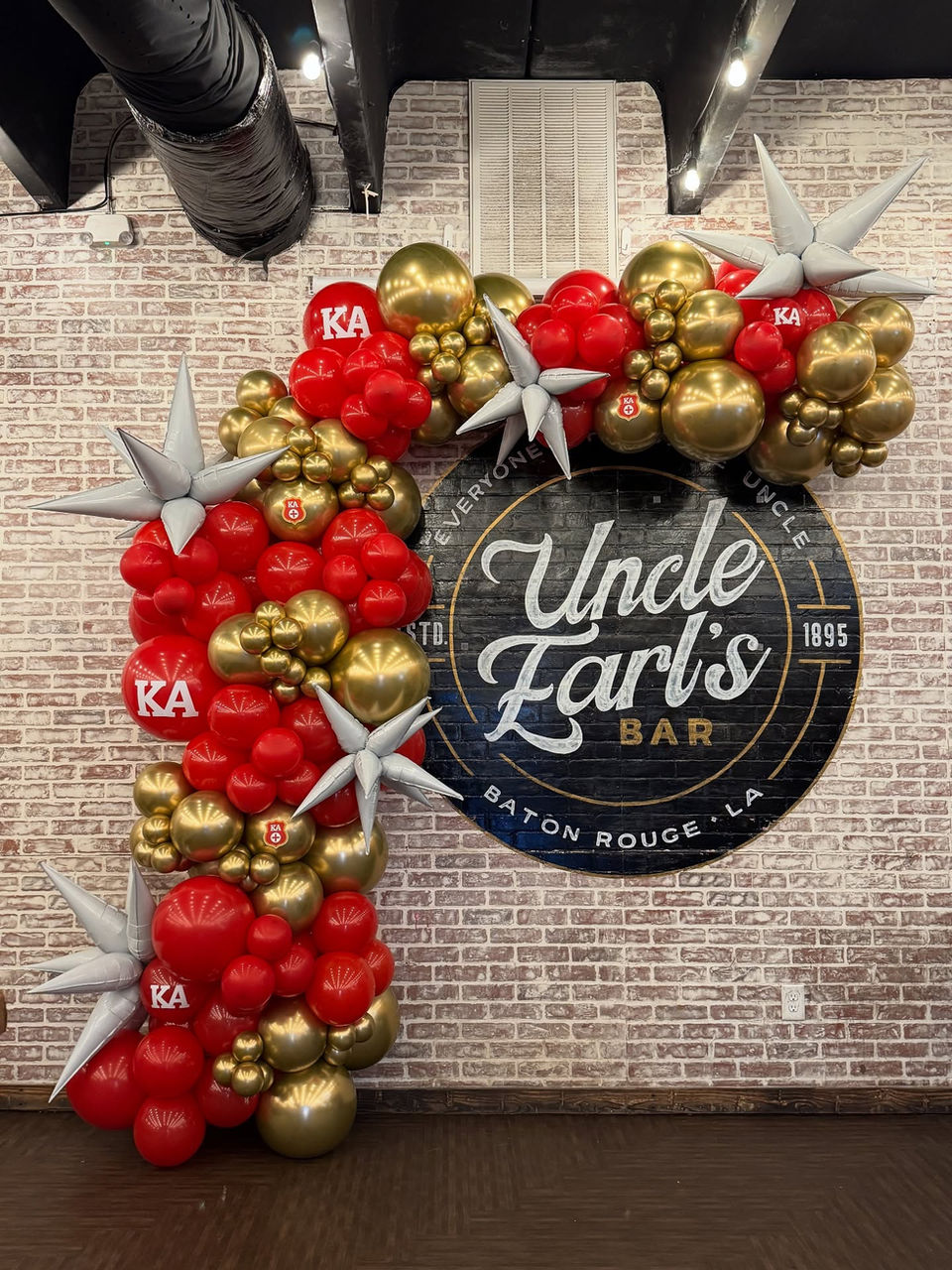 Uncle Earl's BBQ photo backdrop with red and gold balloon garland on the left side going up and over the logo.