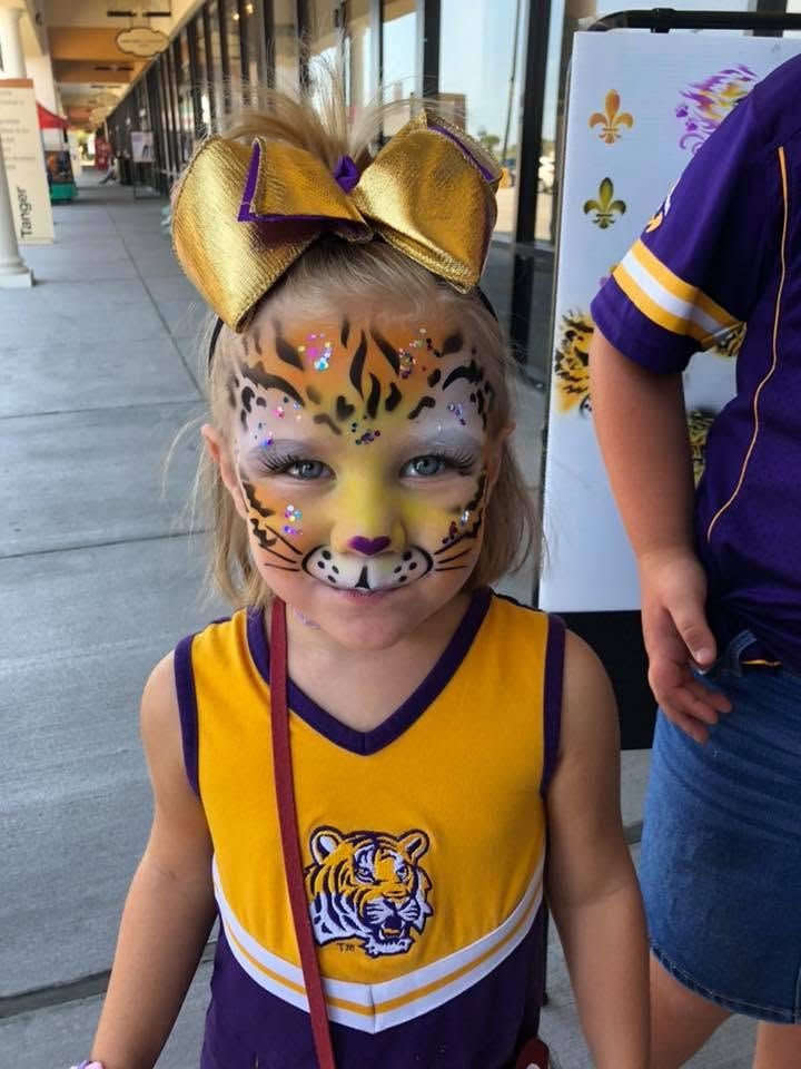 Young girl with LSU cheer outfit on with tiger face paint. 