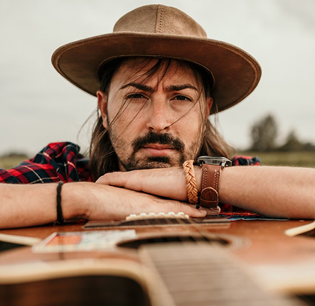 Vertical Shot of a Young Man with a Brown Hat Posing with a Guitar in a Rural Setting (1).
