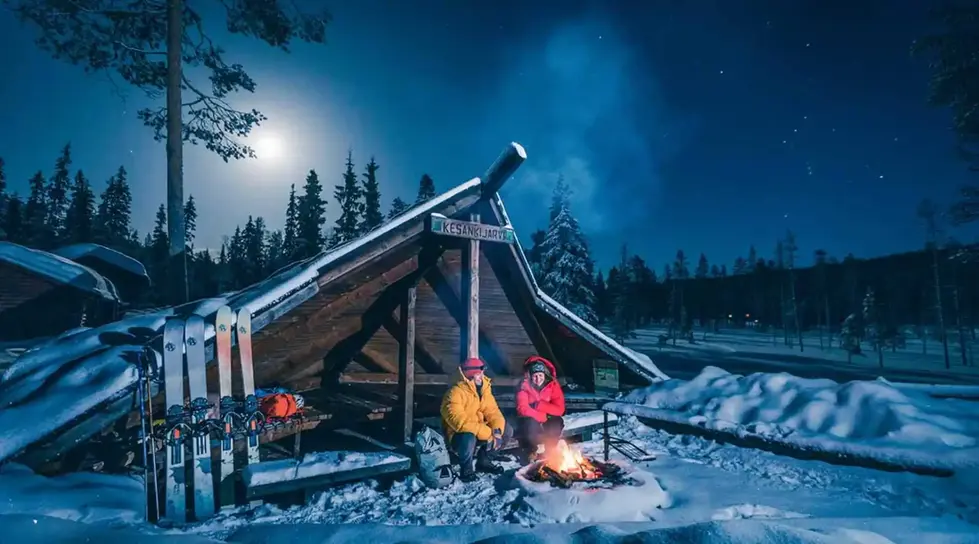 two people sit around a fire under a sign that says kesankajarvi