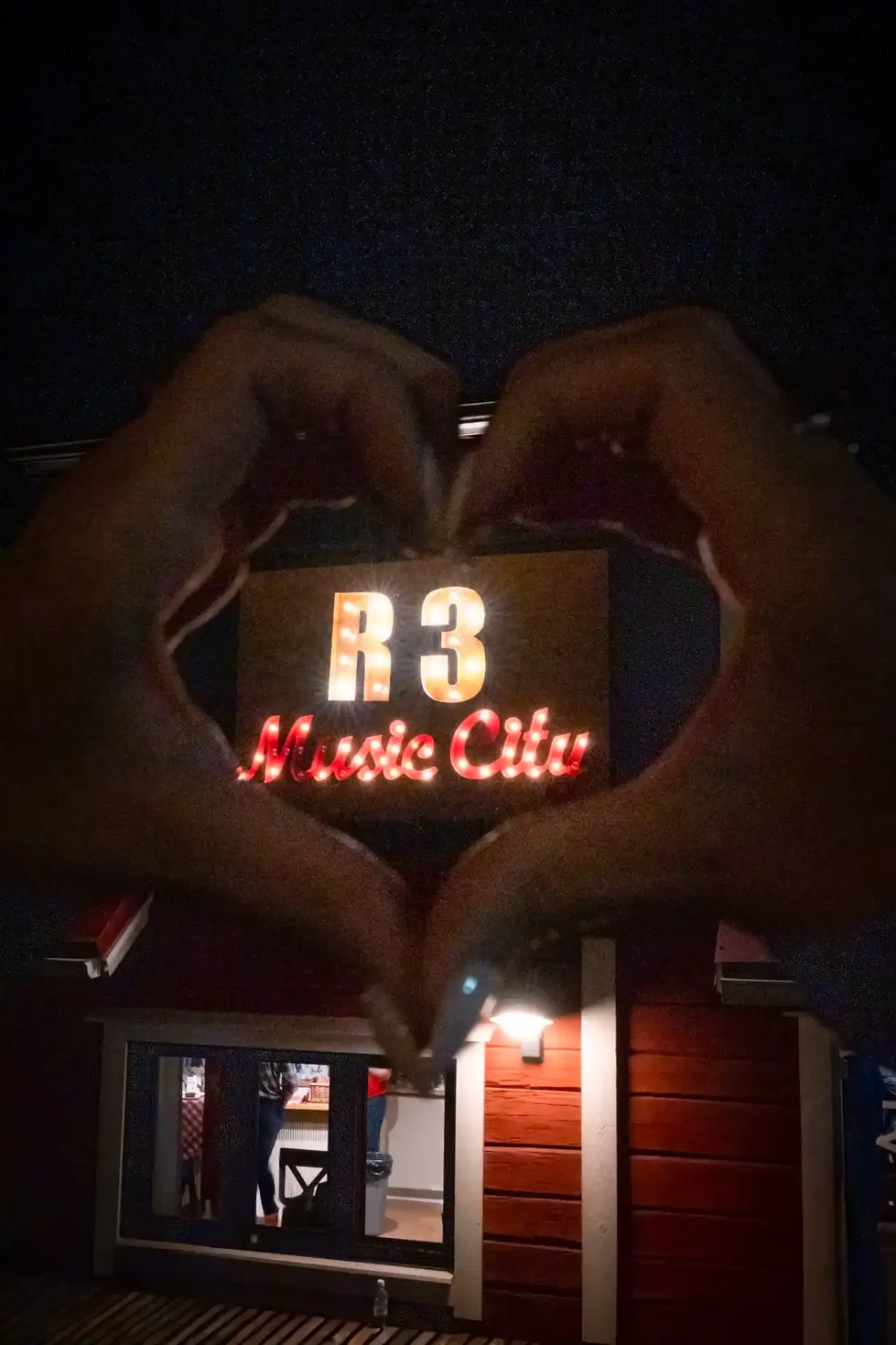 a person making a heart shape in front of a sign that says r3 music city