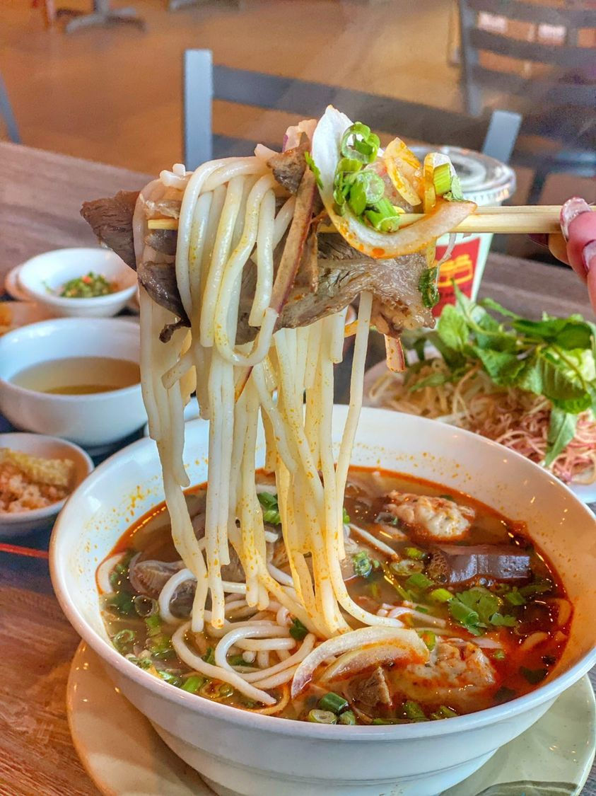 Eye-level view of a bowl of Bun Bo Hue with fresh herbs and lime wedges on the side