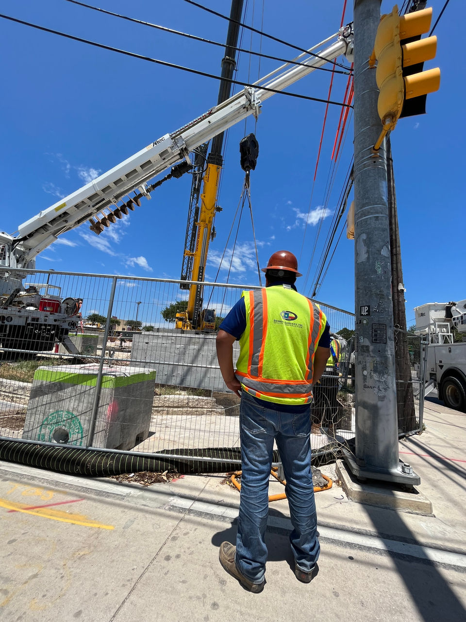 Worker in safety vest and hard hat guiding a crane lift at a utility construction site.