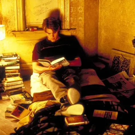 Student sitting on the bed, surrounded by books, reading