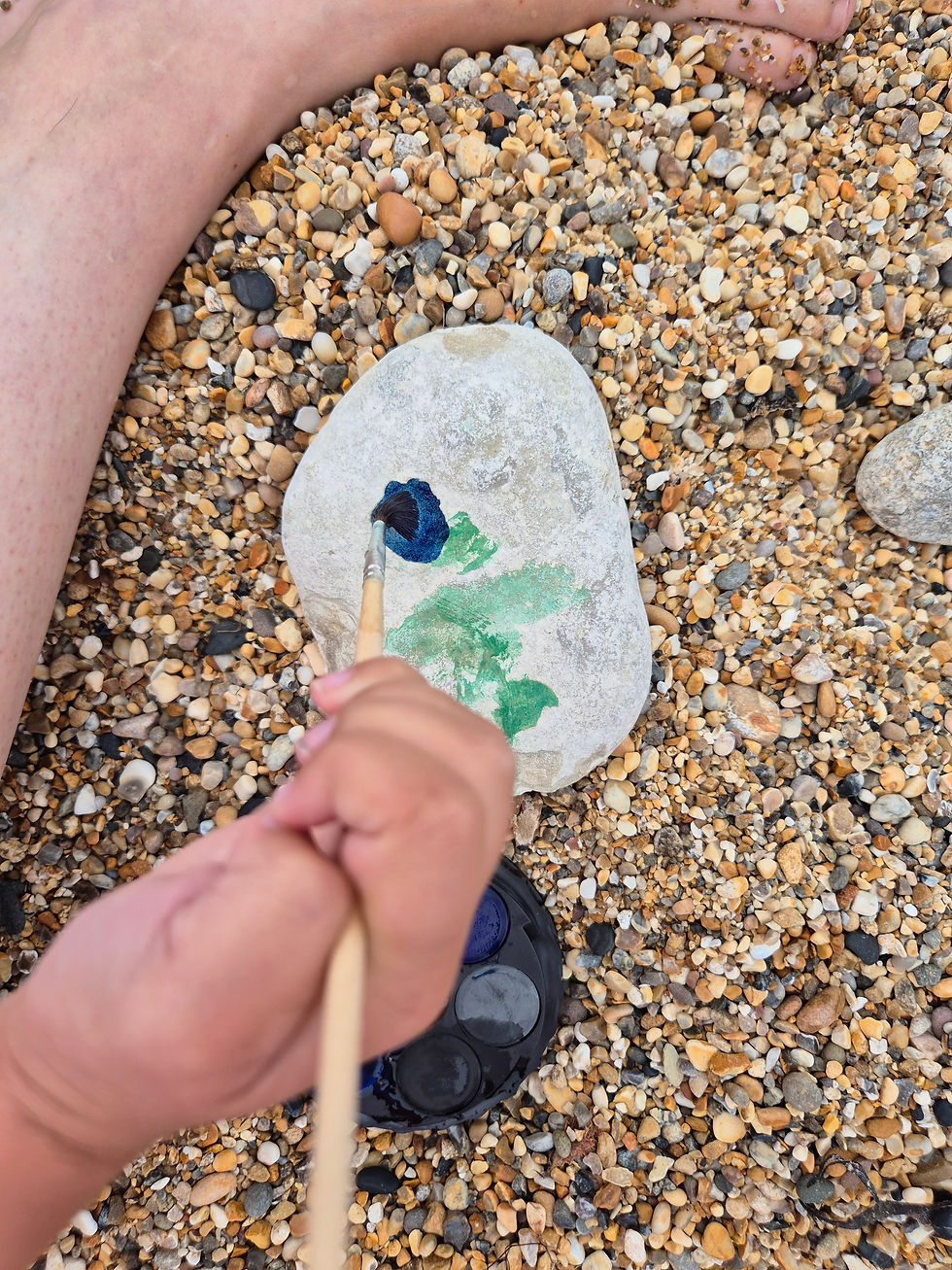 A child painting a pale beach pebble with blue and green watercolours
