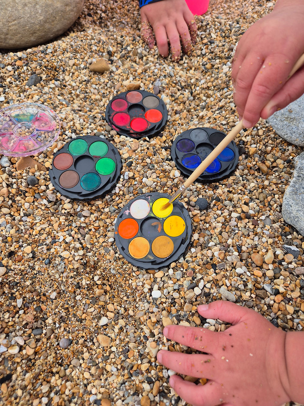Hands dipping a brush into colourful watercolour palettes on the shingle