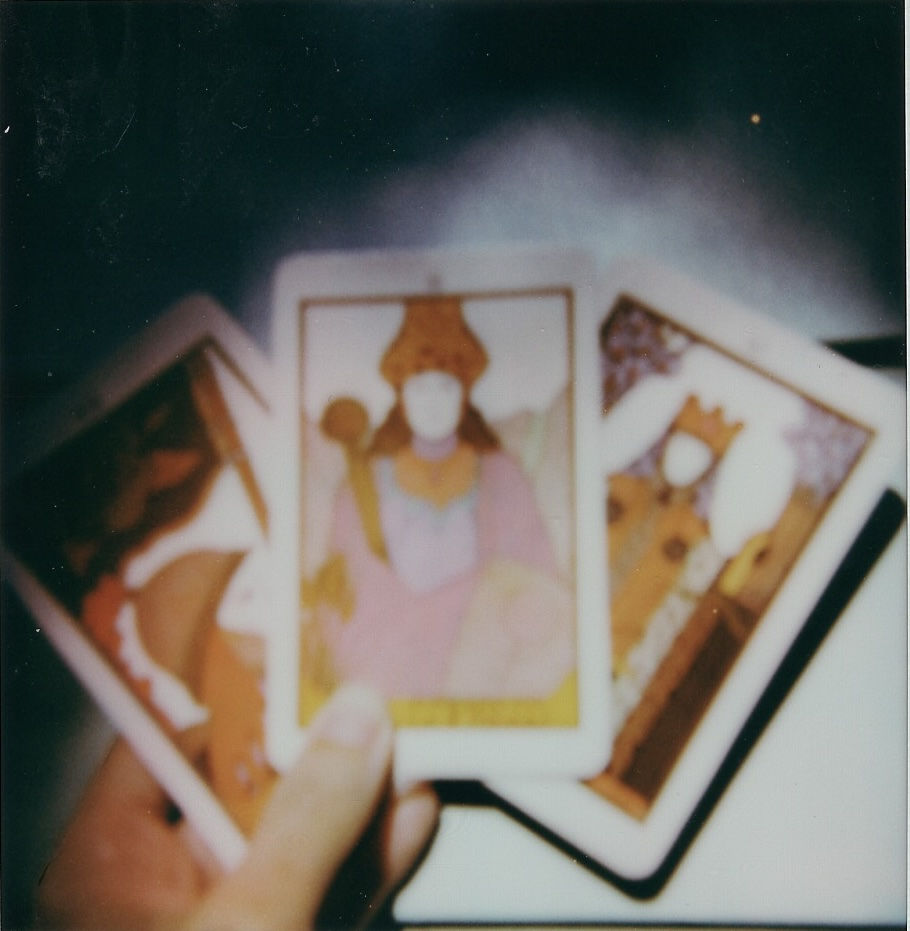 a polaroid of a hand holding 3 tarot cards