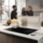 Três pessoas conversando perto do fogão com uma panela de macarrão, e coifa de bancada.