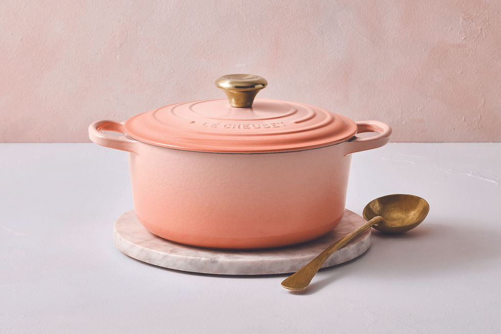 Panela Le Creuset rosa com "LE CREUSET" gravado, sobre mármore, colher dourada.
