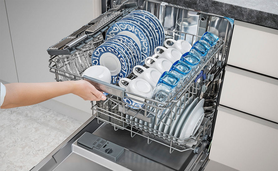 Uma pessoa arrumando pratos, xícaras e copos na lava-louças.