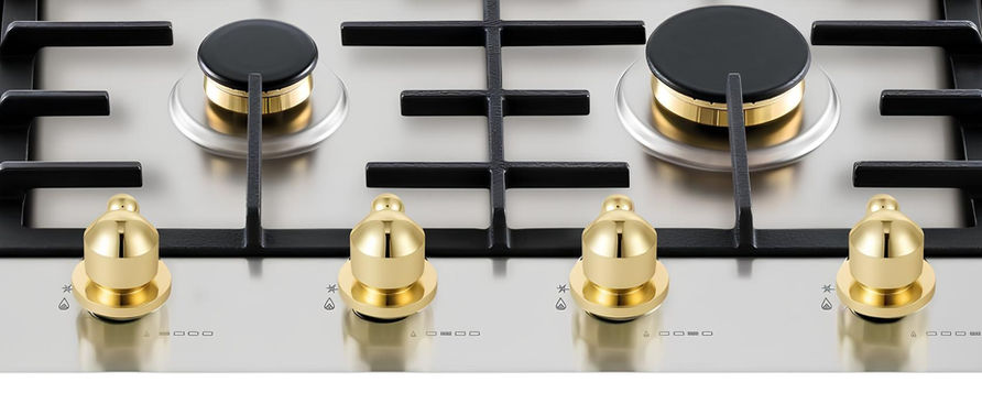 Fogão inox com botões dourados e detalhes inox, vista de perto.