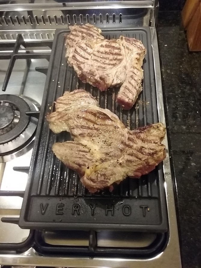 Dois bifes suculentos grelhando em uma chapa quente com texto Very Hot.