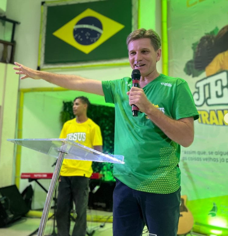 Pastor pregando na Igreja Ilhabela em frente à bandeira do Brasil.