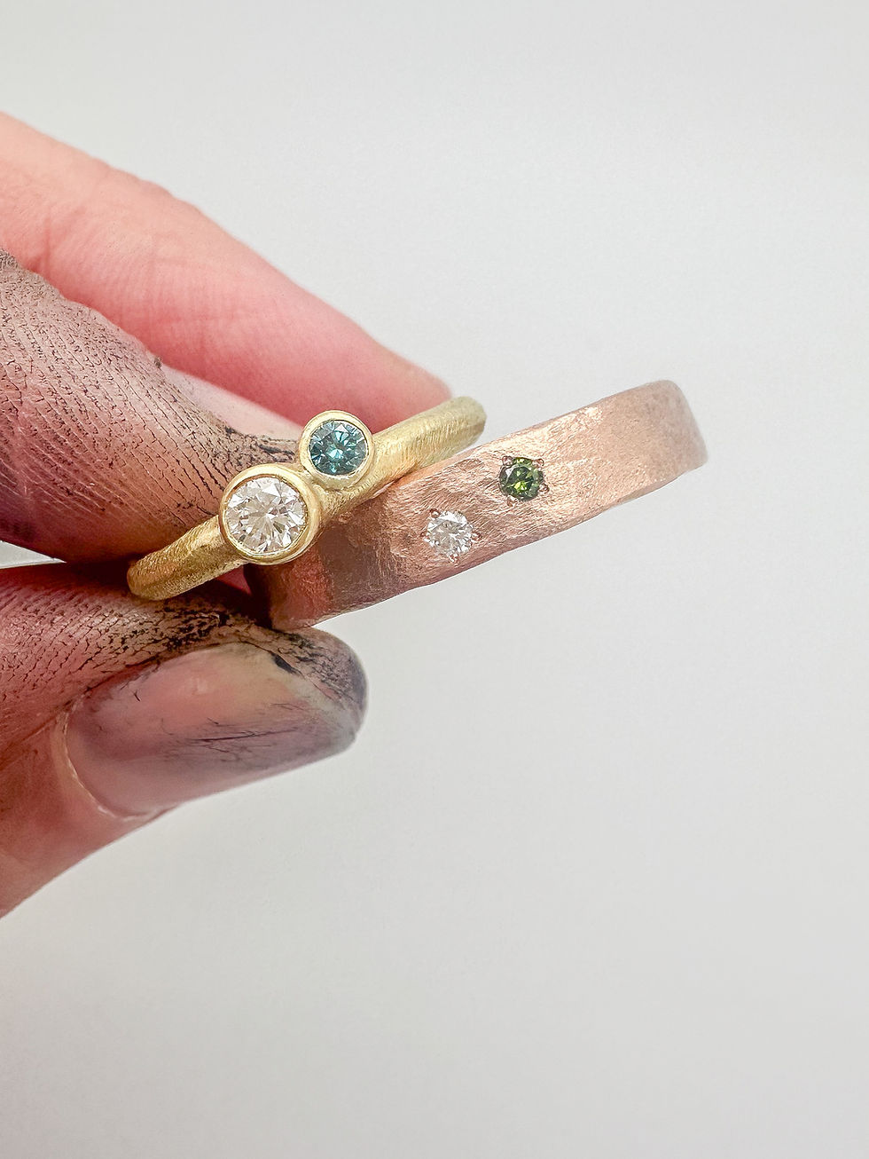 Twee gouden trouwringen: een smalle geelgouden ring met 2 steentjes in opbouw en een iets bredere roodgouden ring met twee steentjes.