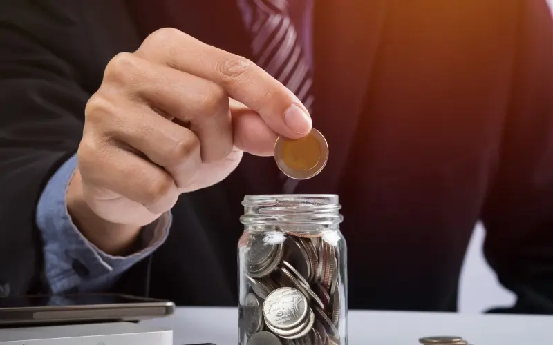 A hand putting mixed coins and seeds in a clear bottle