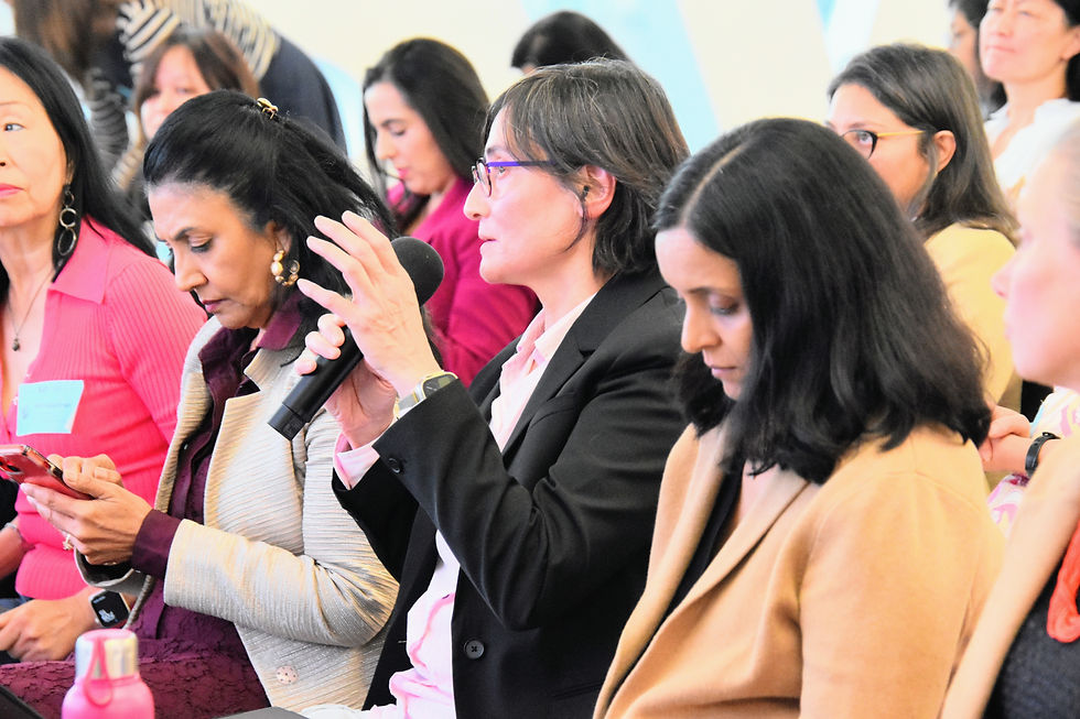 Women seated at a panel discussion, one speaking into a microphone while others listen and take notes in a bright room