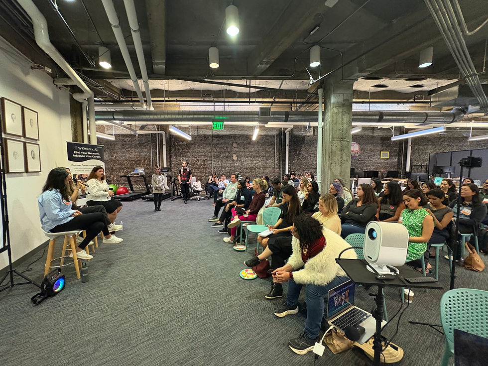 Three people on stools speak to an engaged crowd in a modern, industrial room about building AI products. A sign reads "Women x AI." Attentive audience listens.