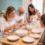 Adults standing around a table and painting pottery and smiling