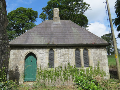 A tiny stone gatehouse. The front door is green, and there are three tall, narrow windows along the front.
