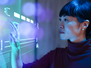 A person interacting with a transparent digital interface, touching on-screen data visualizations and system icons in a blue-lit environment.