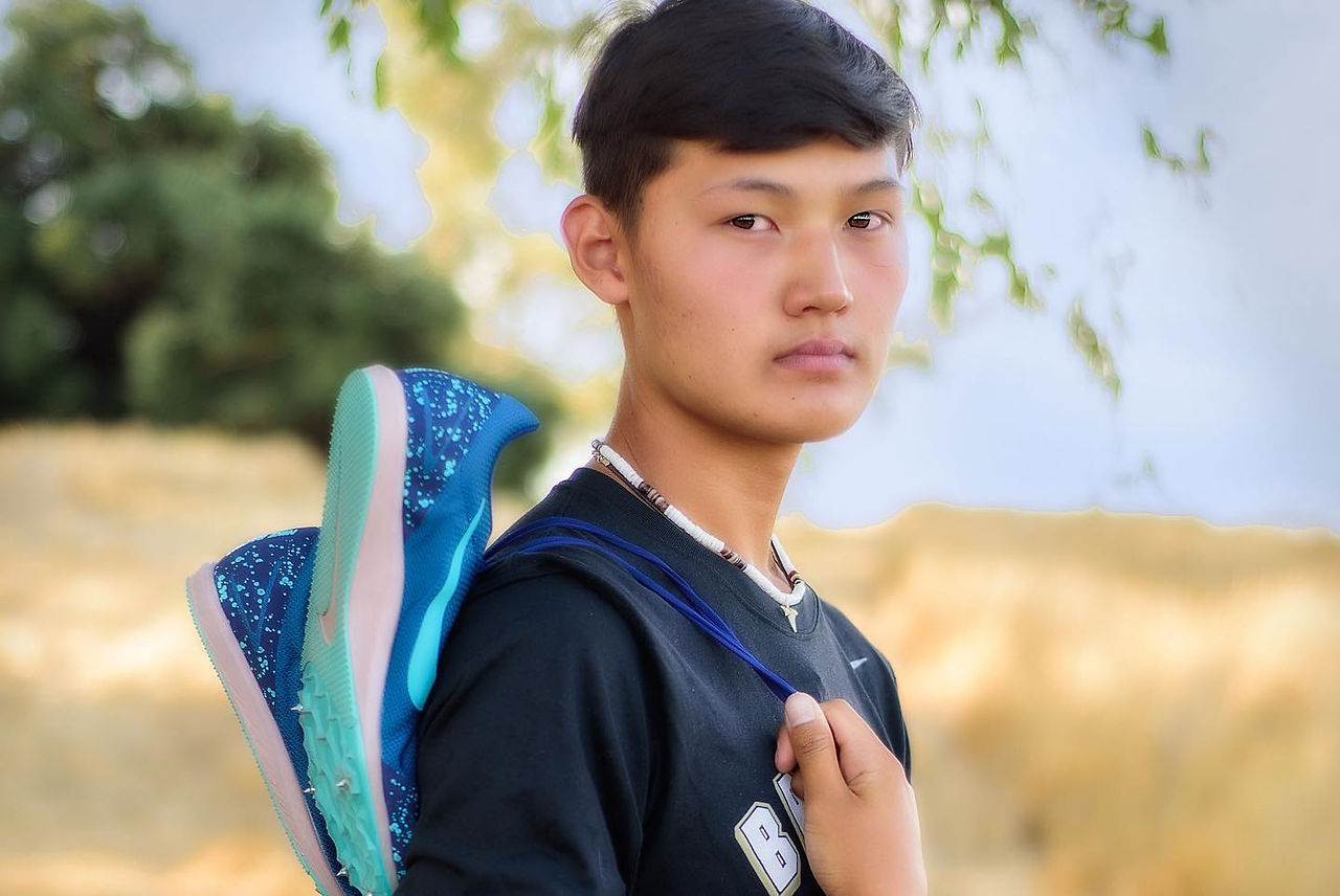 Vista Murrieta high school senior holding his track shoes in a field in Murrieta California