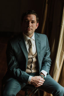 Retrato de Eduardo sentado, con luz lateral y mirada al frente, en una escena elegante y sobria.