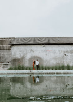 Vista amplia de la pareja a la distancia junto a un muro, con un espejo de agua en primer plano