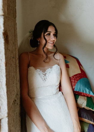 Retrato de Daniela apoyada en una esquina interior, con luz suave y vestido de novia.