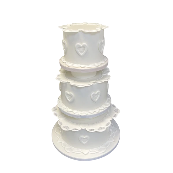 Three-tier white wedding cake with heart motifs and lace-like details.