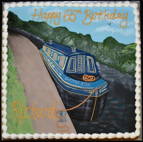 A beautifully decorated cake featuring a detailed narrowboat scene with vibrant colors and intricate designs, perfect for any celebration or special occasion.