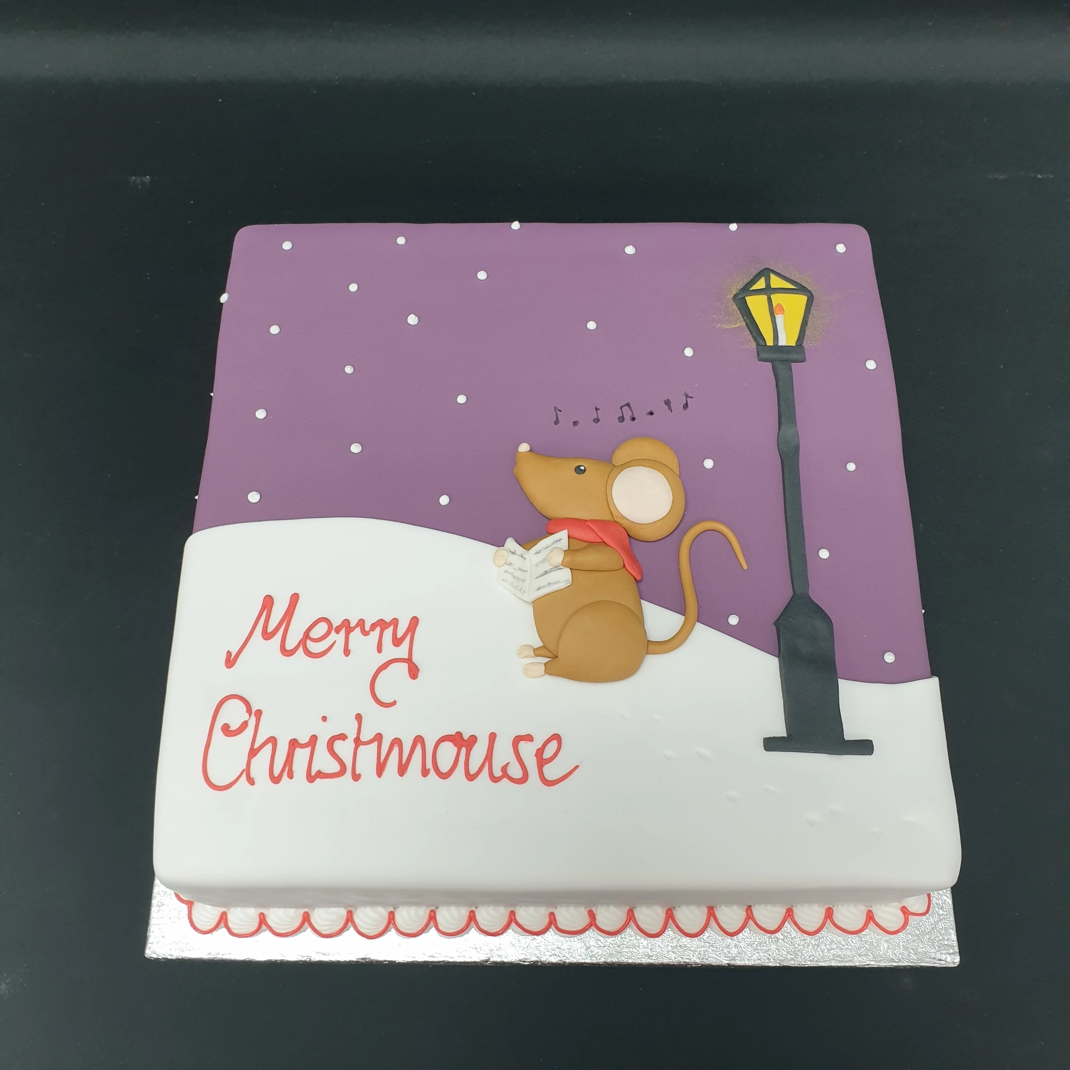 A festive Christmas cake featuring a cute mouse decoration on top, perfect for celebrating the holiday season in style.