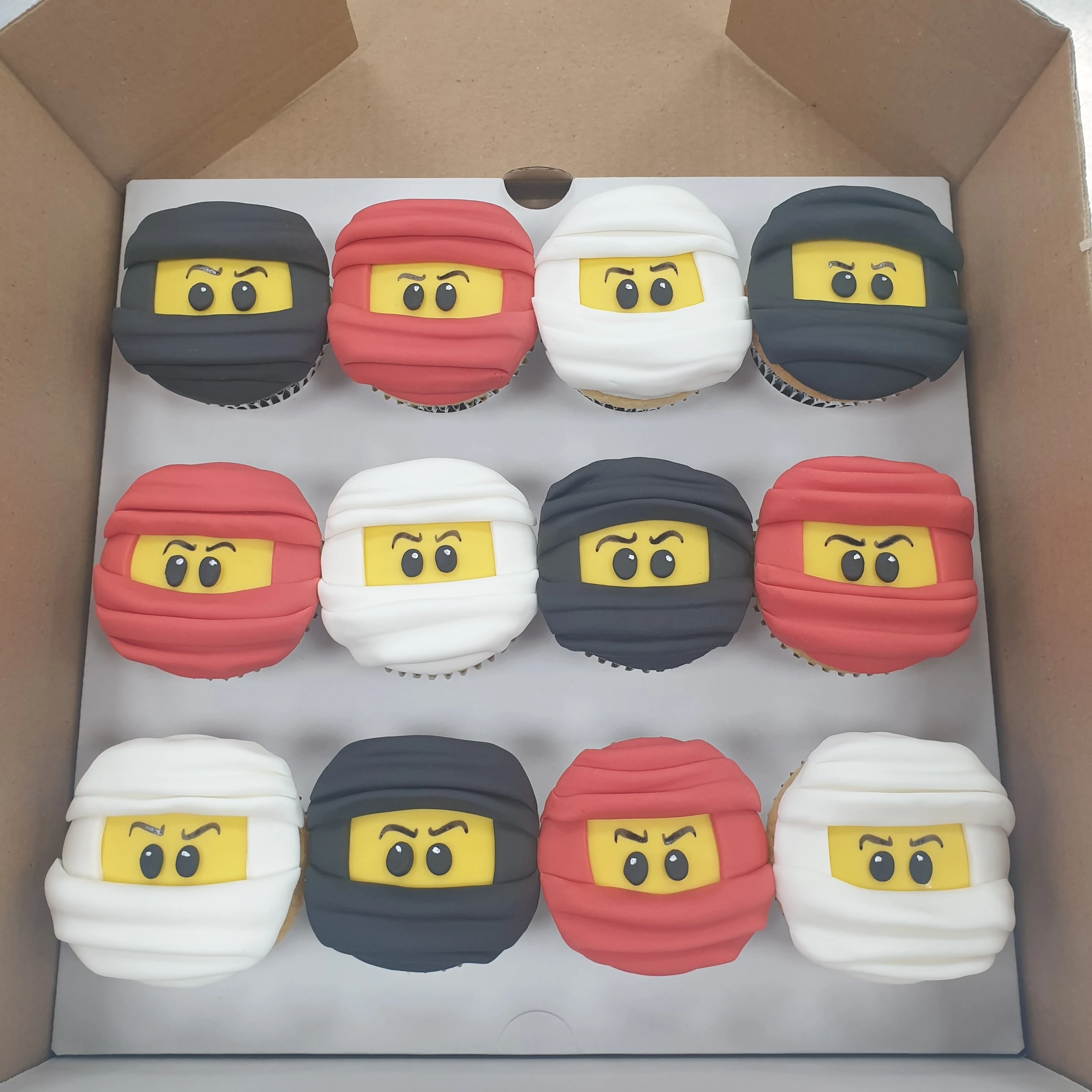 A set of colourful Lego Ninjago themed cupcakes with detailed edible decorations depicting characters and symbols from the popular toy and TV series.
