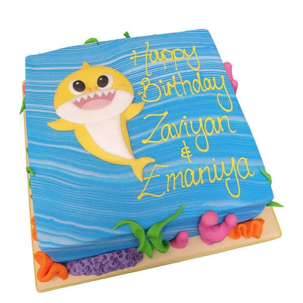 Brightly coloured baby shark-shaped birthday cake with ocean-themed decorations in blues, whites, and yellows. Perfect for a fun and playful celebration!