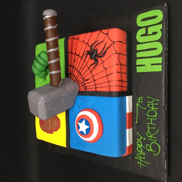 A colourful superhero-themed celebration cake with vibrant decorations and fondant figurines on top, perfect for a themed party or event.